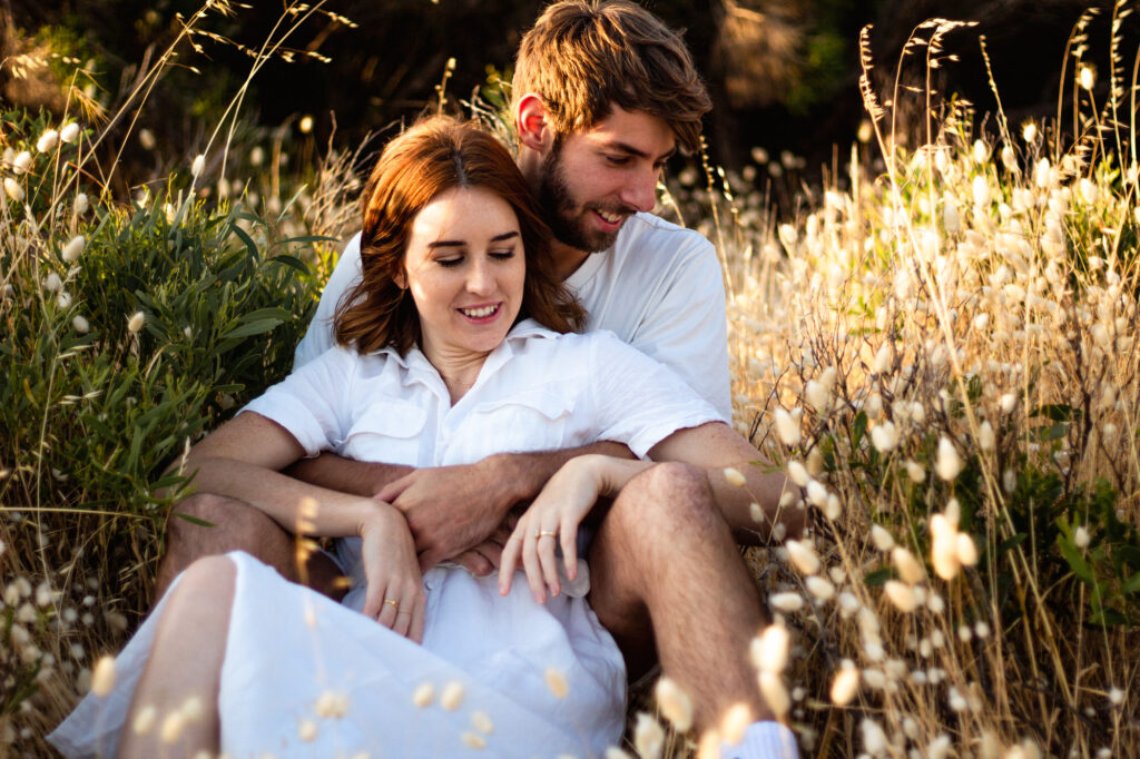 Couple-sitting-in-patch-of-fluffy-dandelions-relaxed-and-holding-each-other