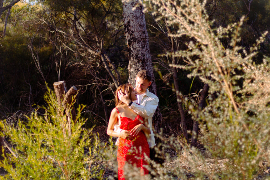 Couple-in-nature-woman-in-red-dress-sharing-an-intimate-moment-with-her-boyfriend-both-looking-at-each-other