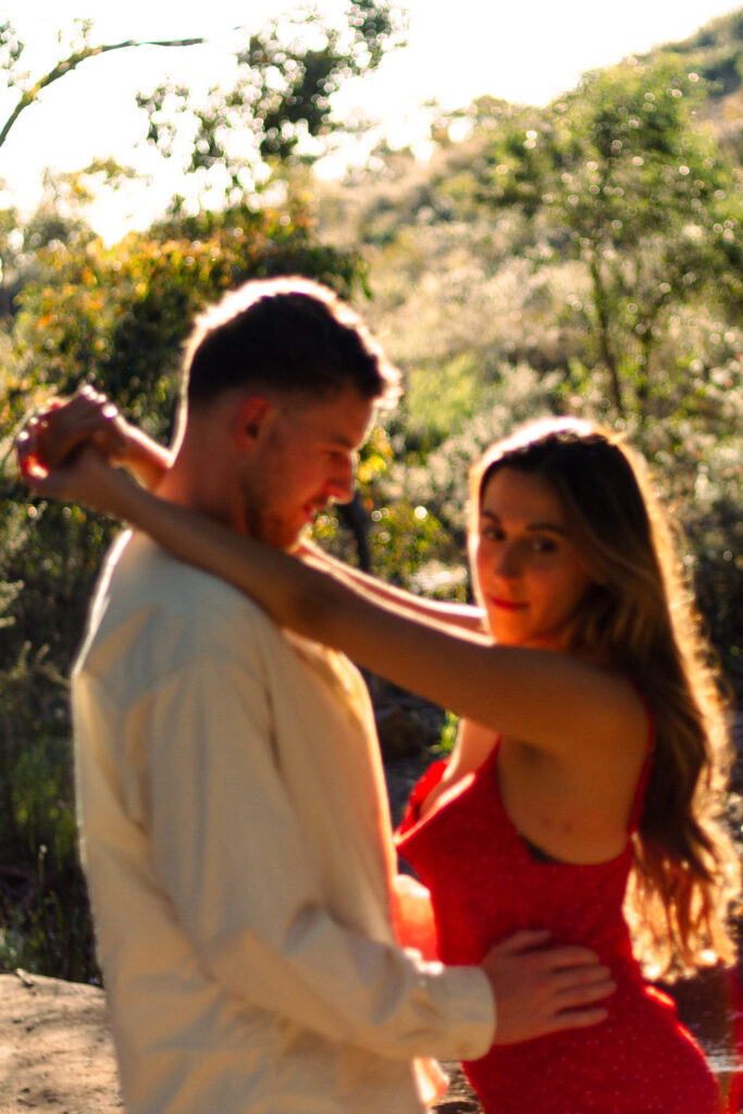 Blurry-shot-of-couple-at-golden-hour-womans-arms-resting-on-mans-shoulders-as-he-holds-her-waist